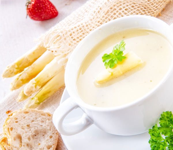 Spargelcremesuppe serviert mit Brot und Petersilie.