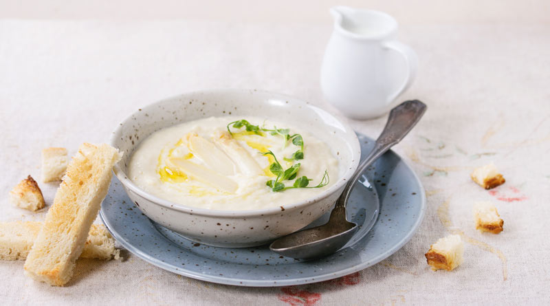 Spargelcremesuppe serviert mit Brot und Sahne.